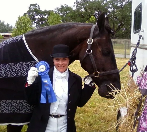 A rider in show attire holding a blue ribbon beside a black Friesian, Hendrik