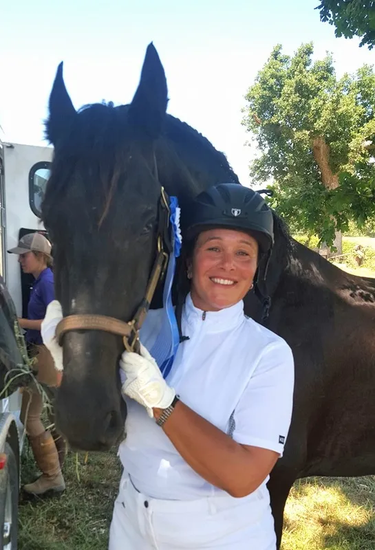 A rider in show whites beside Johan, a black Friesian, with a ribbon