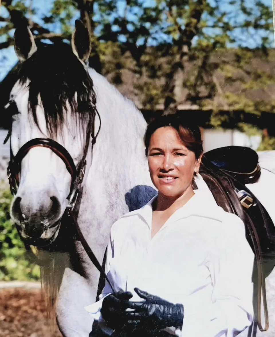 Portrait of Tressa Boulden standing beside a tacked grey horse